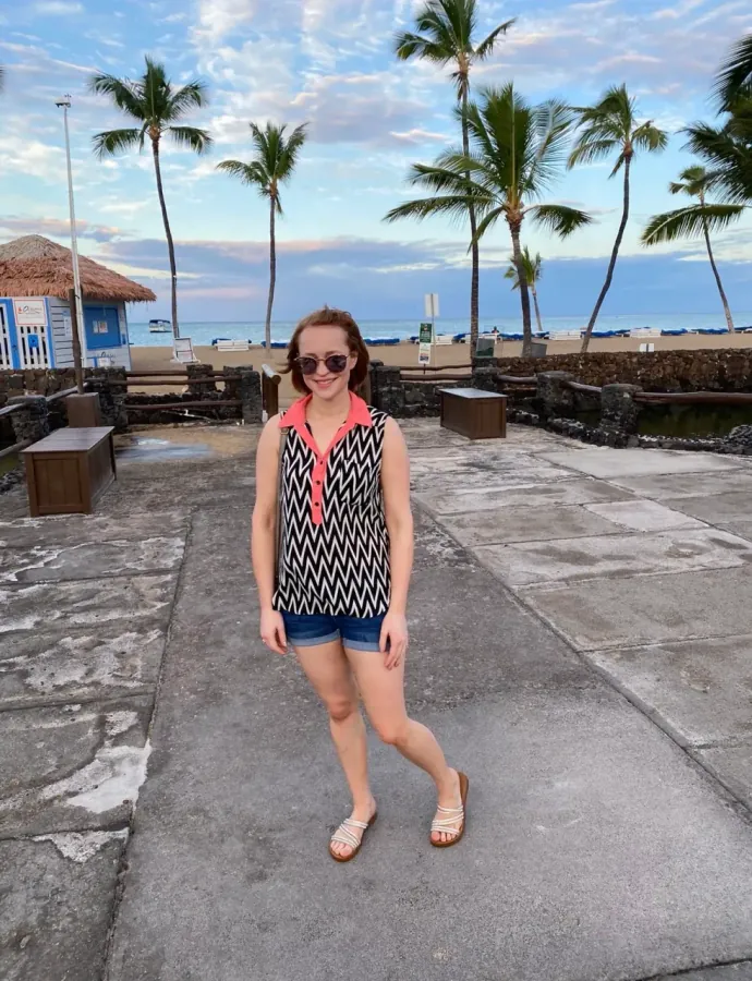 Hannah Burke on vacation, standing on a beachfront walkway lined with palm trees